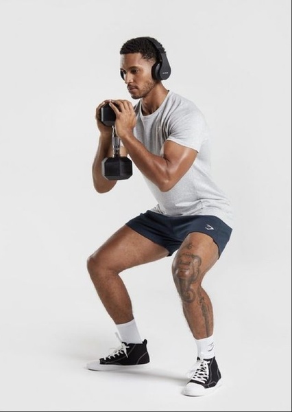 A clean, studio-lit shot of a male athlete performing a goblet squat with a single dumbbell, using high-contrast lighting to emphasize form.
